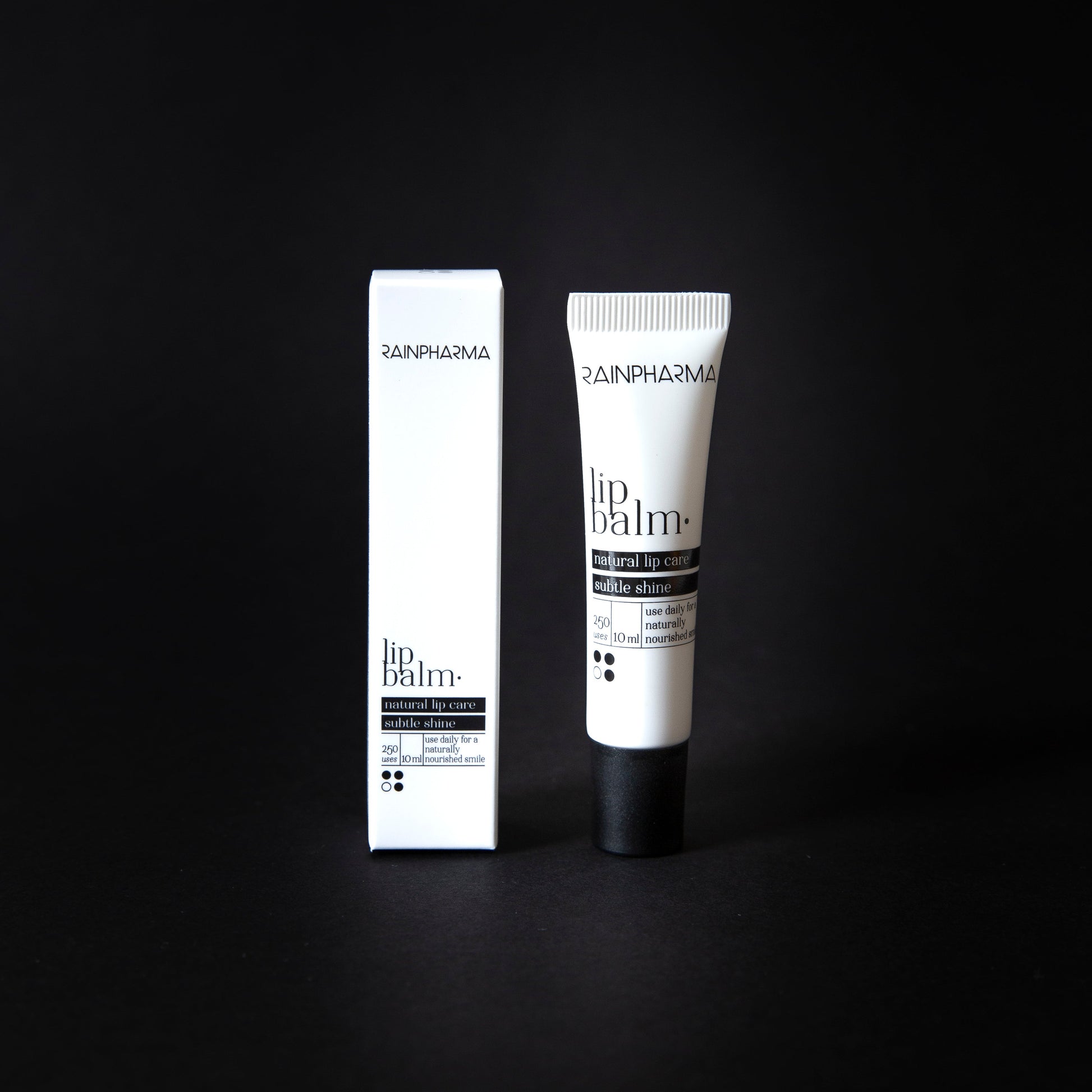 Een RainPharma lippenbalsem, verrijkt met plantaardige oliën, wordt naast de witte verpakking op een zwarte achtergrond getoond.