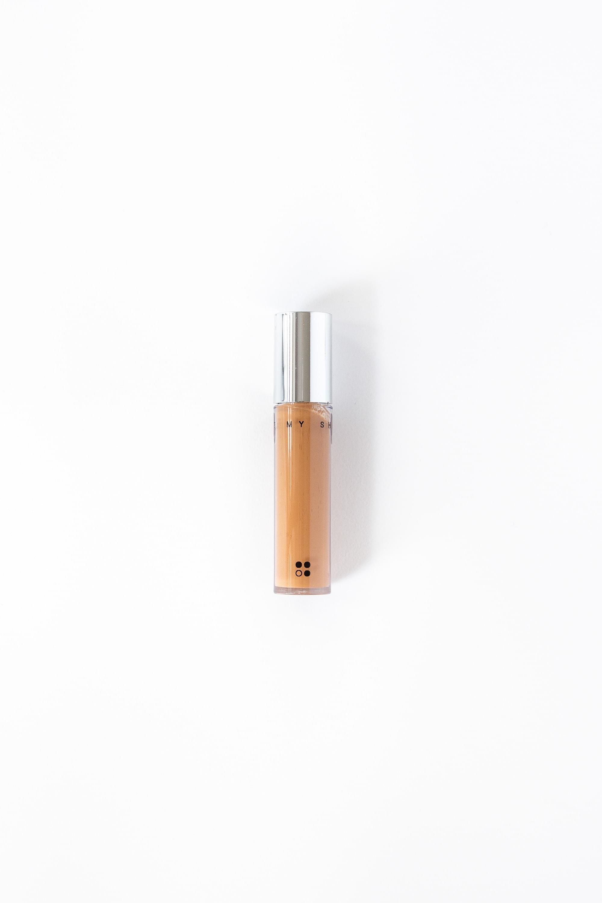 De natuurlijke concealer "Light my Shadow" van RainPharma, met een veganistische formule, wordt verticaal afgebeeld op een witte achtergrond en wordt geleverd in een klein flesje met een zilveren dop.