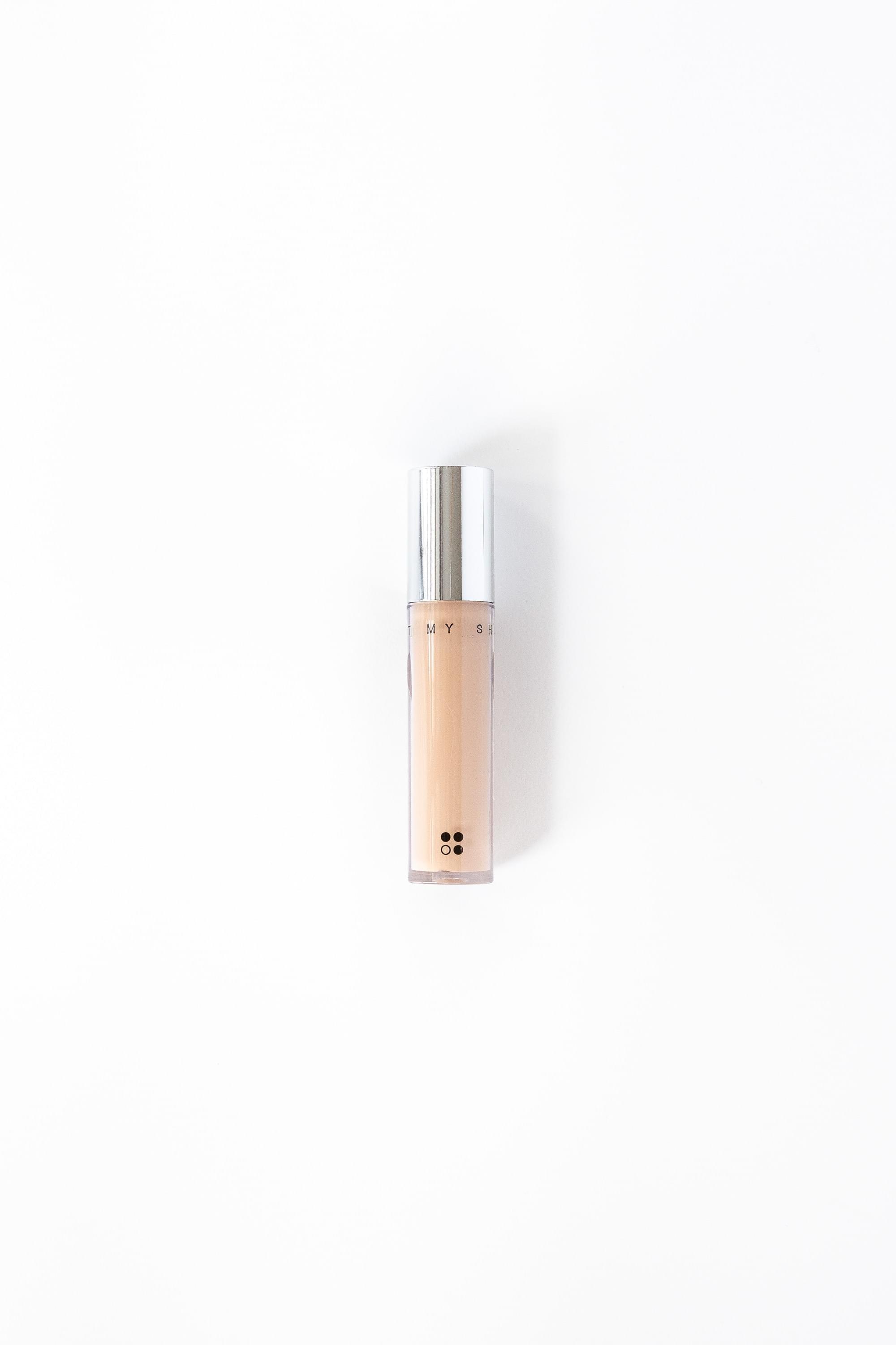 De "Light my shadow" Natural Concealer van RainPharma is een beige vloeibare concealer met een veganistische formule, verpakt in een cilindrische tube met een zilveren dop, verticaal weergegeven op een effen witte achtergrond.