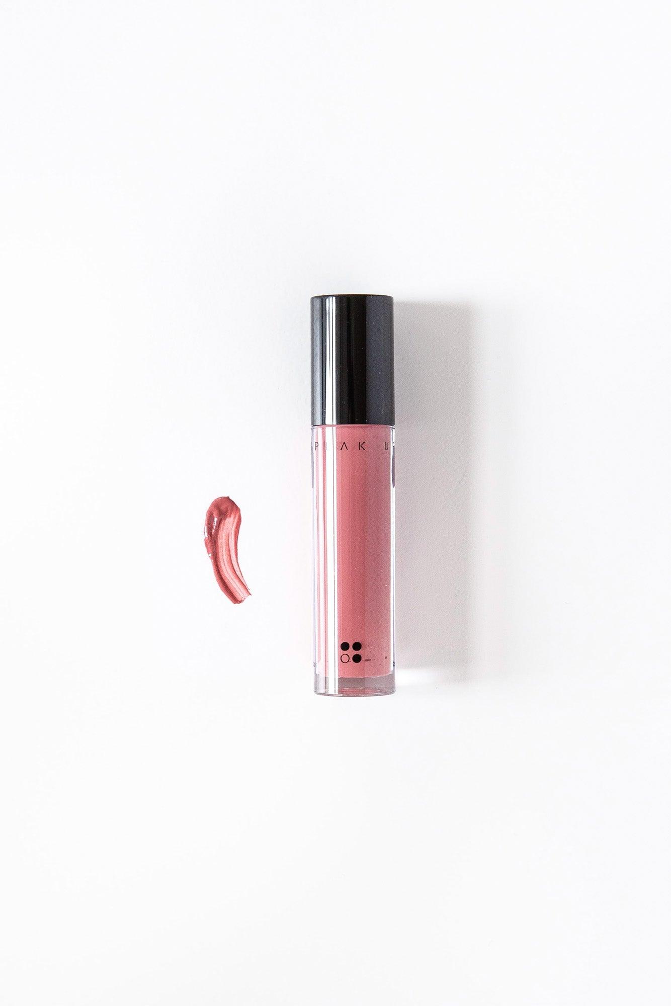 Een tube Speak Up - Natural Lip Tint van RainPharma in de kleur roze met een zwarte dop staat verticaal op een witte achtergrond, met links een veegje van dezelfde glanzend gepigmenteerde kleur.