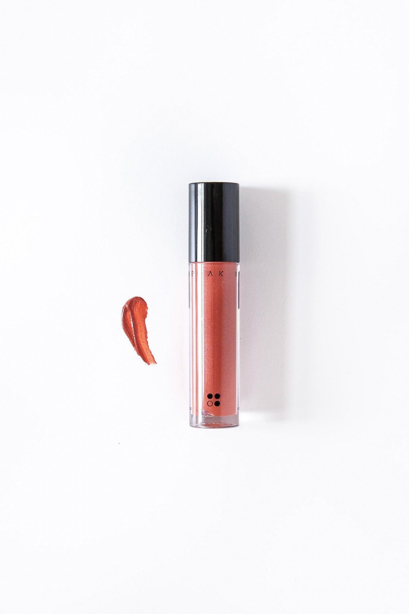 Een tube Speak Up - Natural Lip Tint van RainPharma, in een glanzende metallic rode tint, met een sample op een witte achtergrond, waardoor de glanzend gepigmenteerde glans wordt benadrukt.