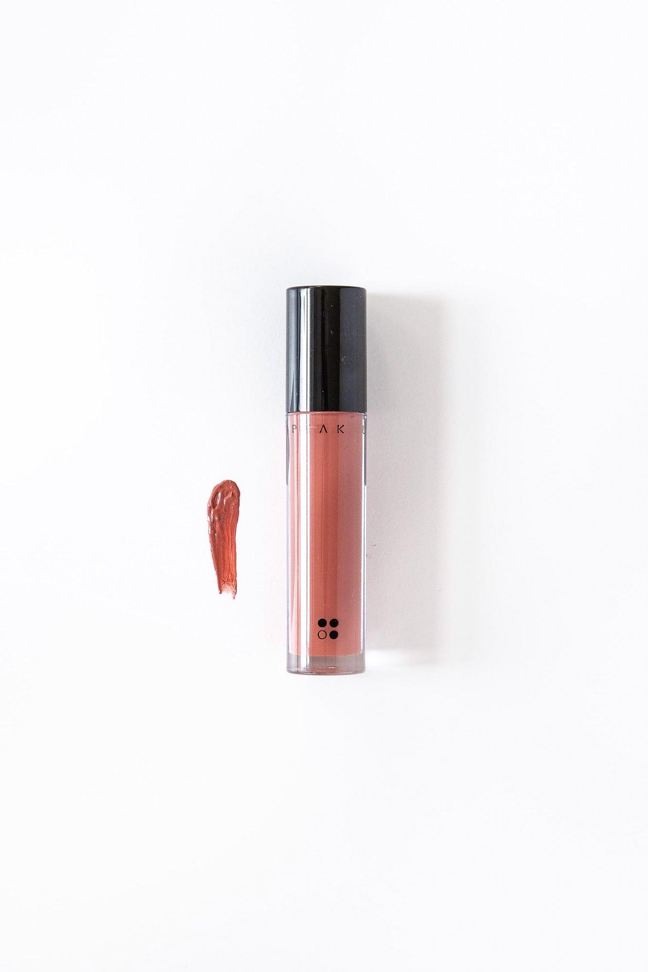 De Speak Up - Natural Lip Tint van RainPharma, met zwarte dop, is naast een swatch van de rijke bruine tint op een wit oppervlak geplaatst, wat zorgt voor een glanzend gepigmenteerde finish.