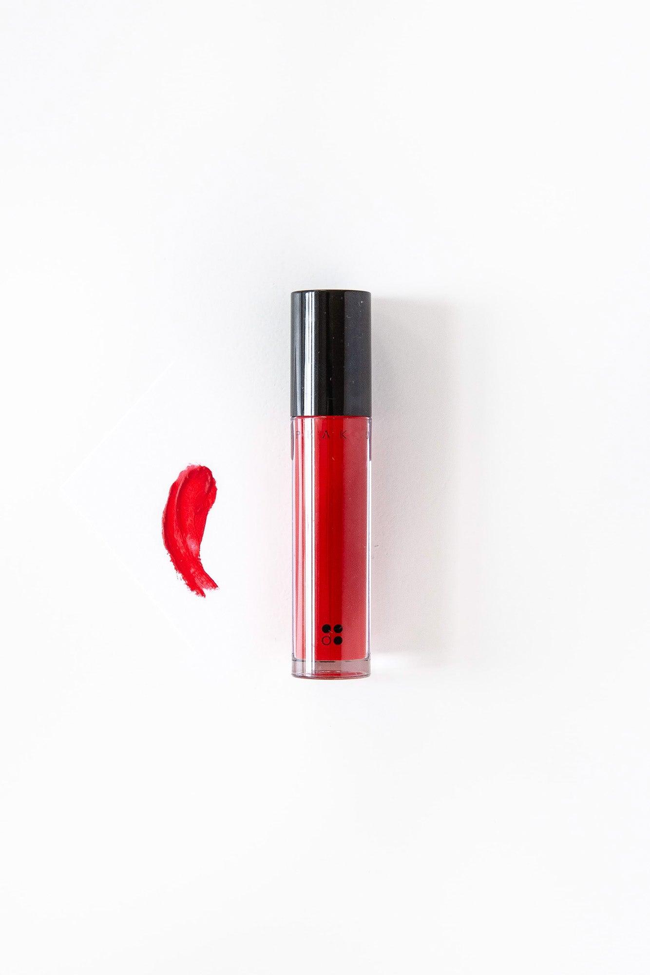 Een tube Speak Up - Natural Lip Tint van RainPharma, veganistisch en met een zwarte dop, ligt naast een opvallende rode veeg op een witte achtergrond, met een lipglossapplicator voor nauwkeurige applicatie.