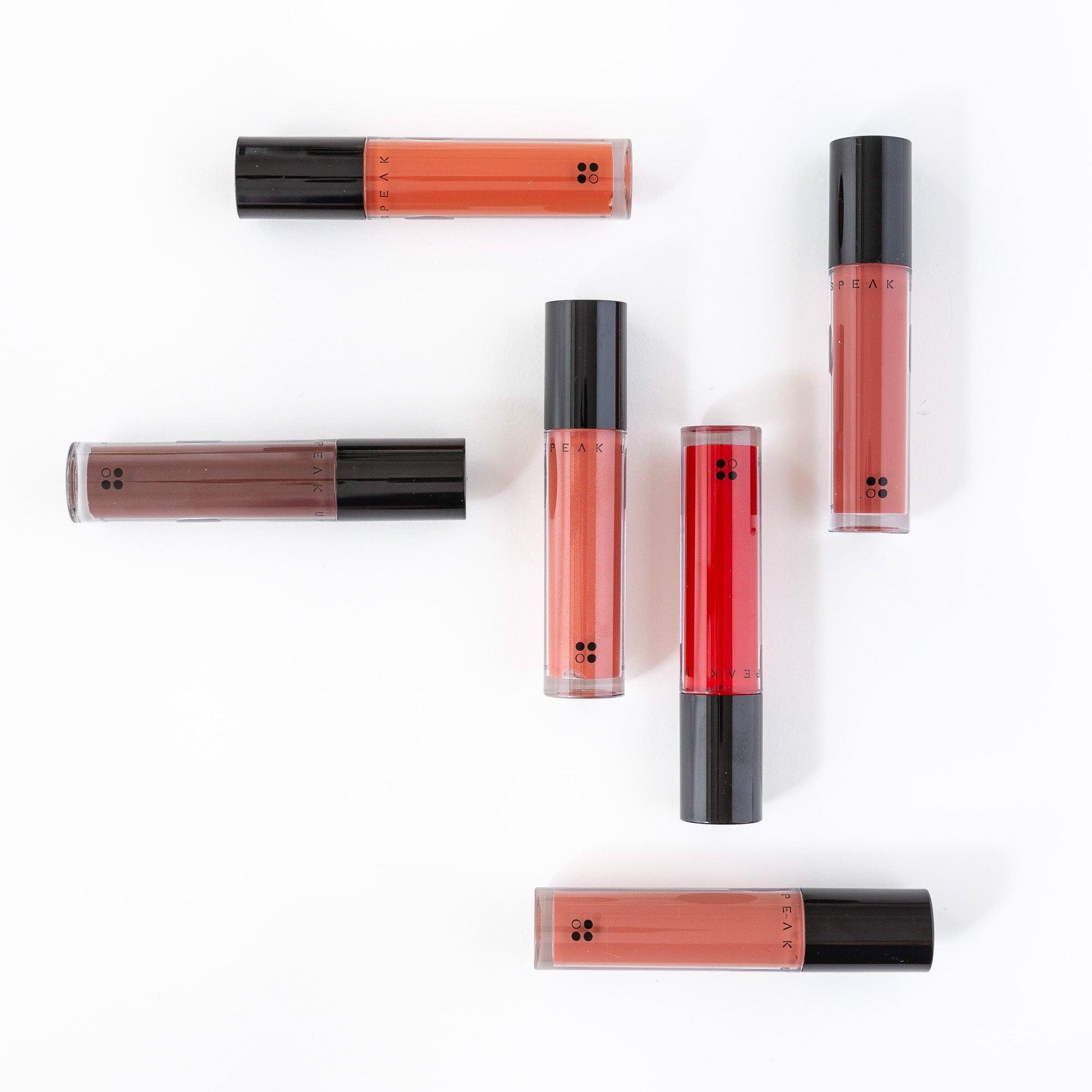 Zes tubes Speak Up - Natural Lip Tint van RainPharma, met zwarte applicators en een glanzende, gepigmenteerde finish in tinten van bruin tot rood, zijn gerangschikt op een witte achtergrond.