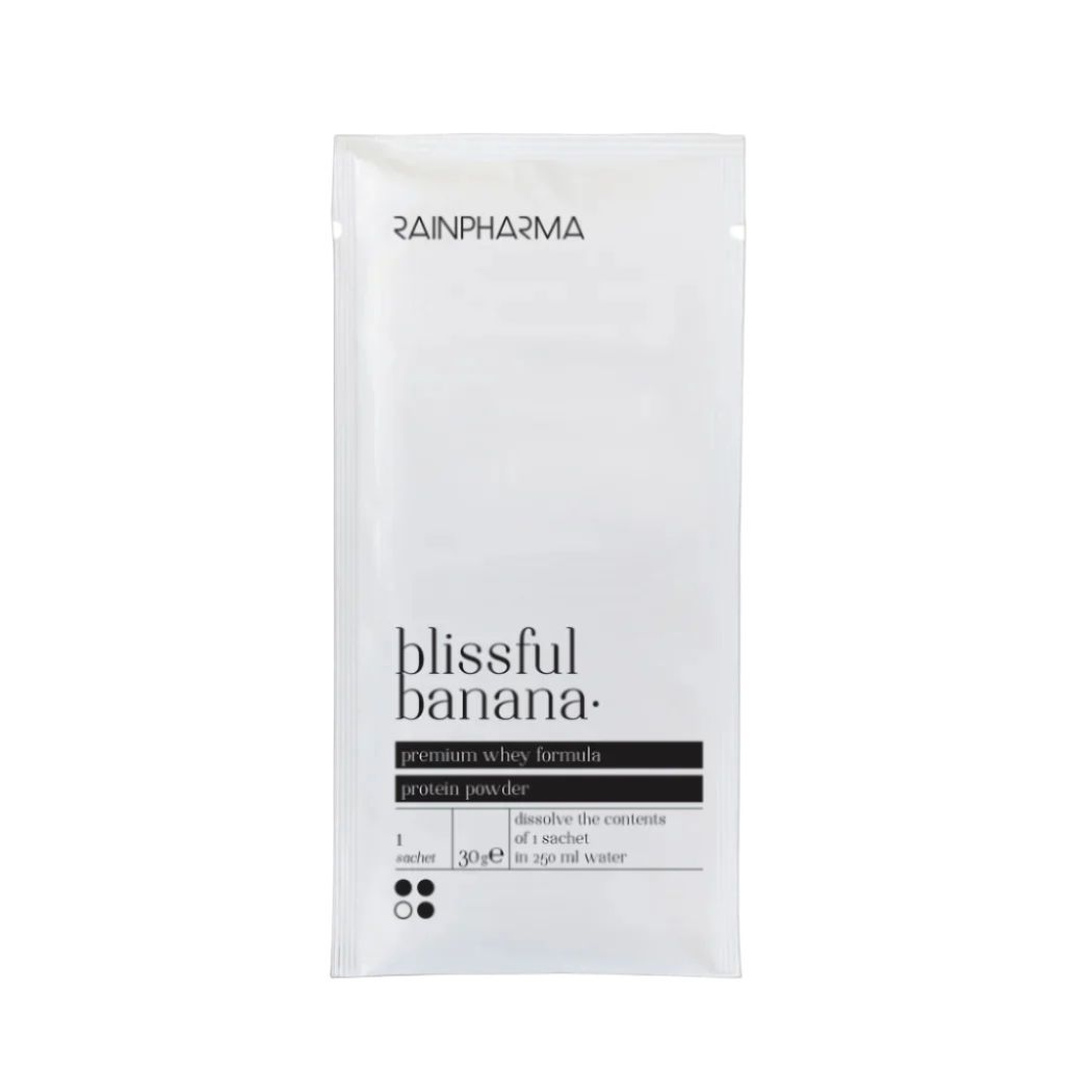 Een wit zakje met het opschrift "RainPharma Shake Blissful Banana Zakjes" met bananensmaak en instructies voor het oplossen van één eiwitrijk tussendoortje in 200 ml water.