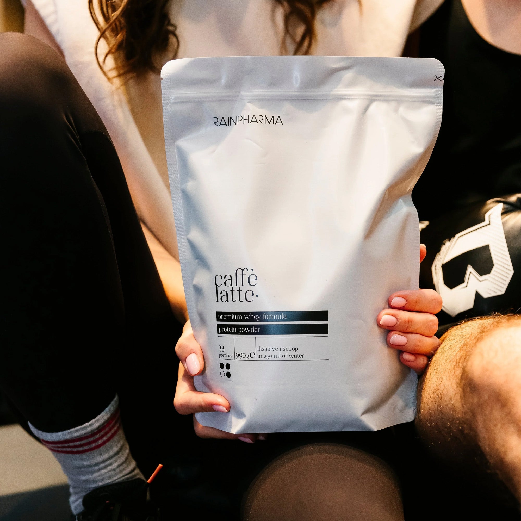 Een persoon die een XL Shake Caffè Latte - 33 porties van RainPharma vasthoudt, ideaal voor een gluten- en caseïnevrij, eiwitrijk tussendoortje.