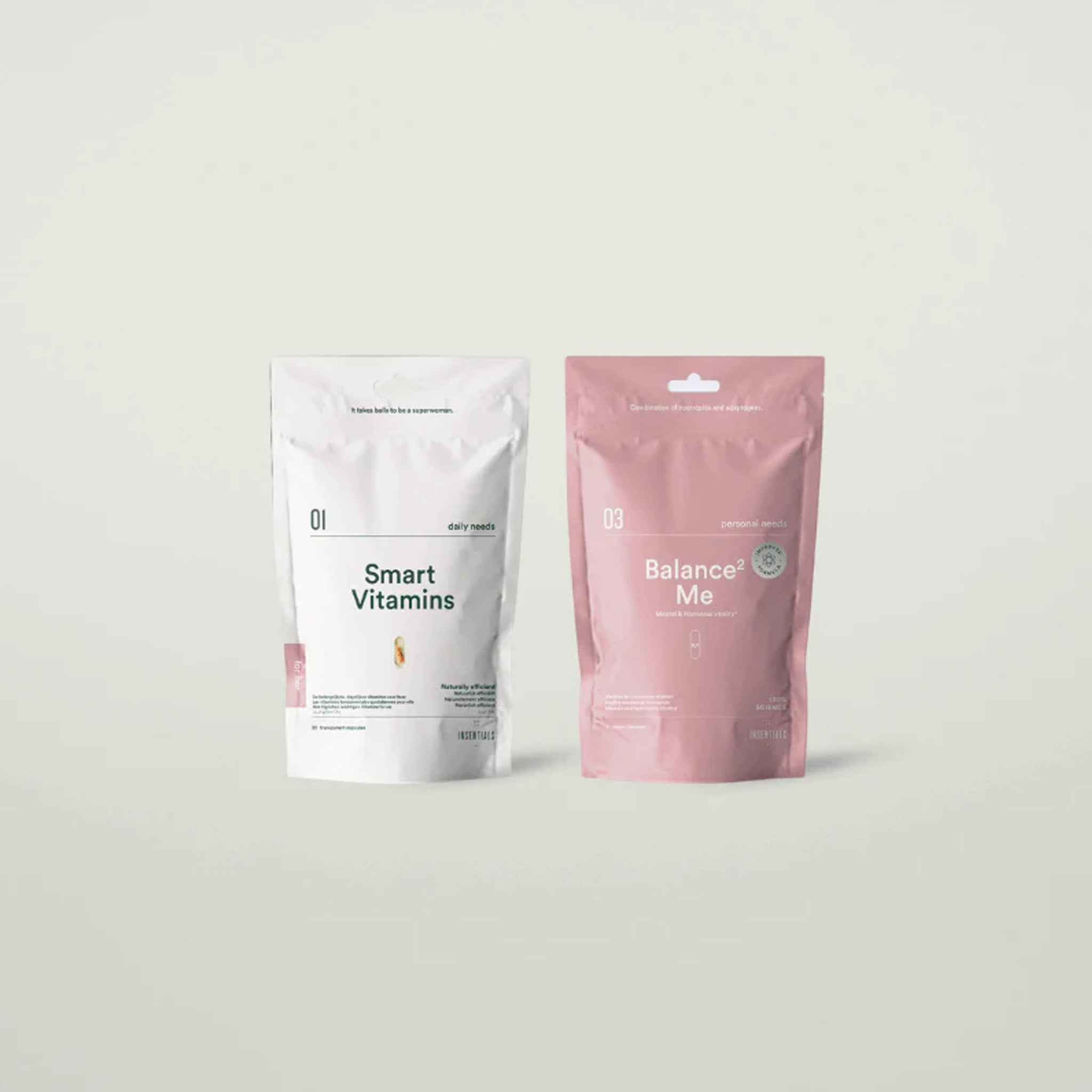 Twee staande zakjes uit het Hormonal Balance Pack van Insentials, één wit met het label "Smart Vitamins" met Adaptohormonal C™ en de andere roze met het label "Balance Me", worden naast elkaar getoond. De zakjes benadrukken de ondersteuning van de hormoonbalans.