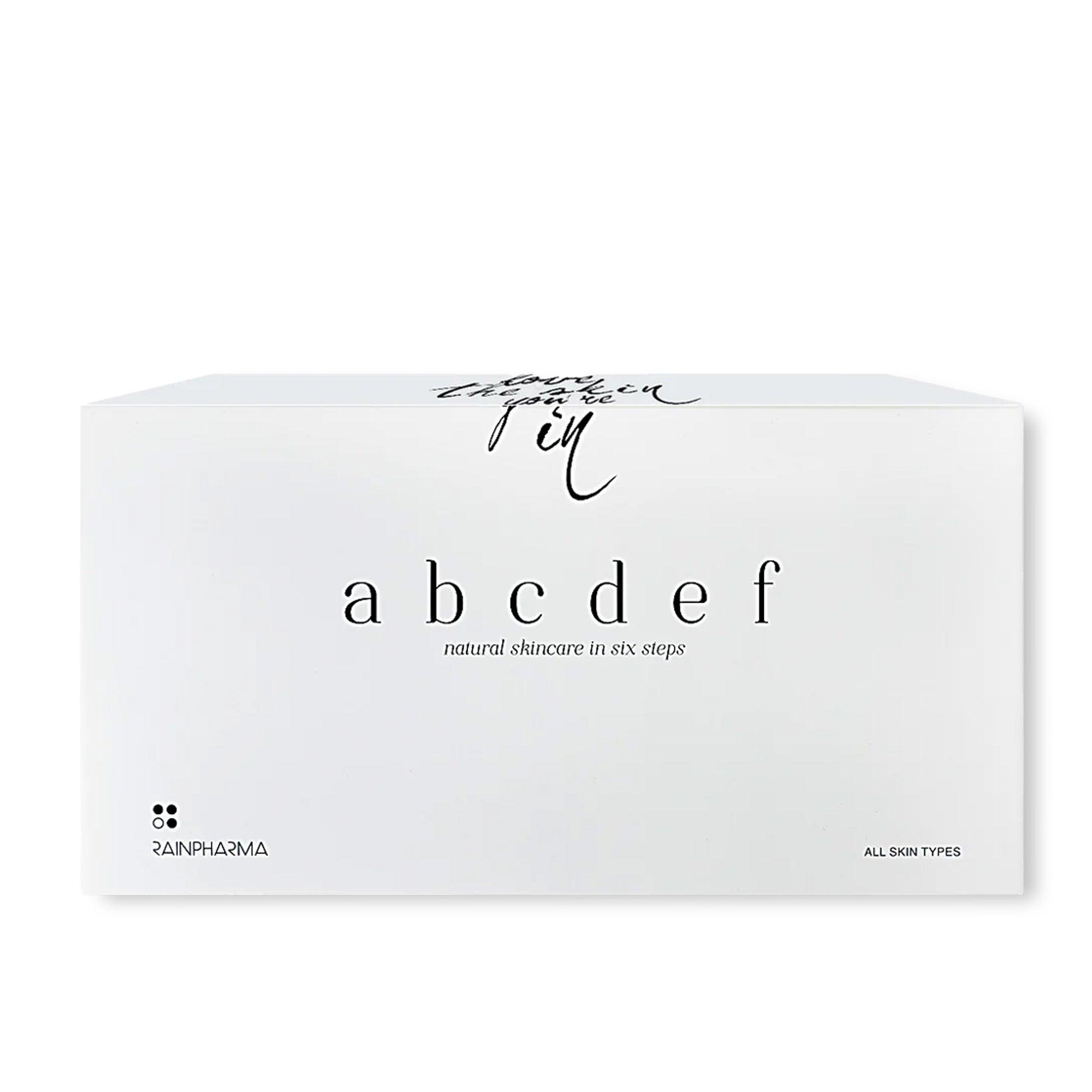 Een wit vak heeft elegante zwarte tekst met "Complete Skincare set - abcdef promobox 4+2 GRATIS" en "natuurlijke huidverzorging in zes stappen", wat een holistische benadering benadrukt. De merknaam, RainPharma, staat linksonder en toont de toewijding aan natuurlijke huidverzorging.