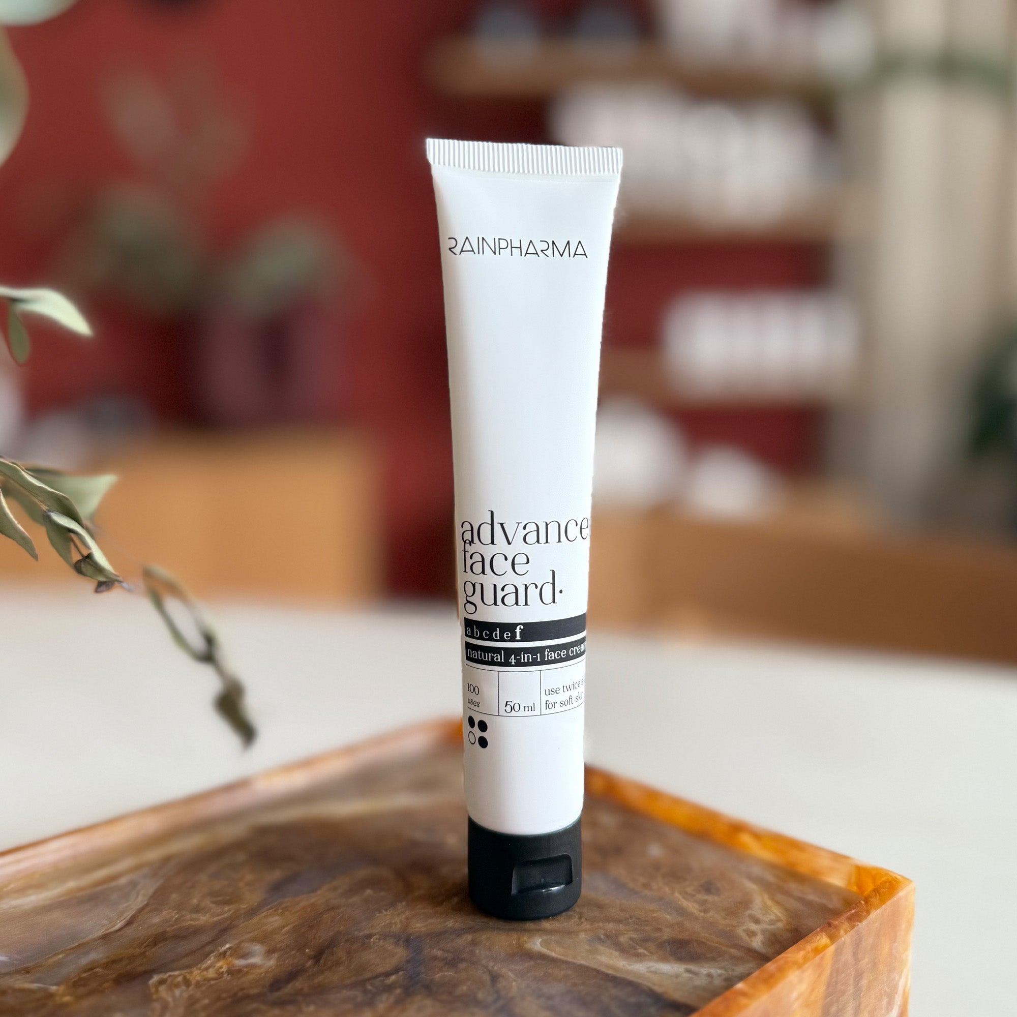 Een tube RainPharma Advanced Face Guard - NEW staat rechtop op een bruin oppervlak, met een onscherpe achtergrond binnenshuis.