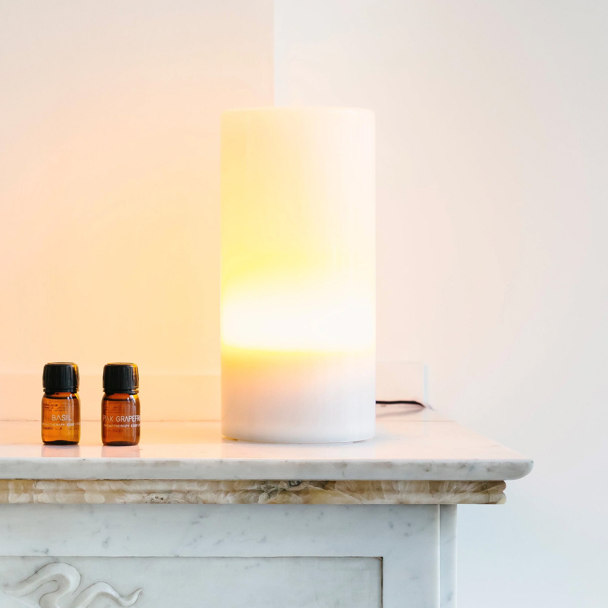 De Aroma Diffuser Set van RainPharma, met Aurora Base en Moonlight Glass Sleeve, staat op het marmeren oppervlak naast twee kleine flesjes met de labels "basilicum" en "six flowers". De stijlvolle diffuser maakt gebruik van ultrasone technologie om de kamer te vullen met een kalmerende geur.