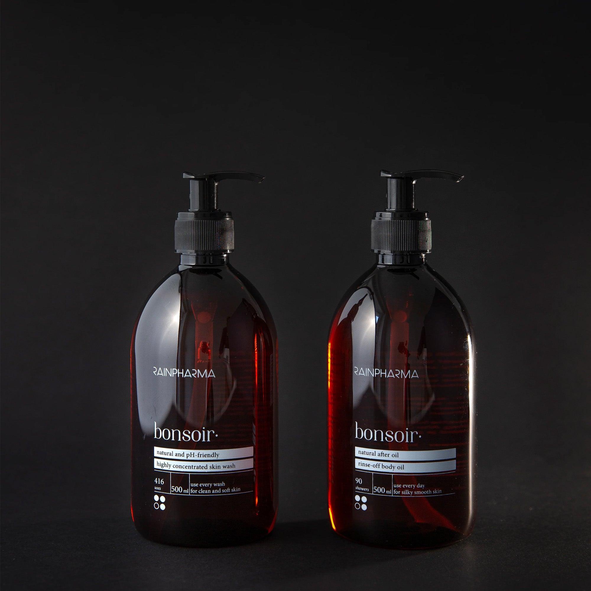 Twee donker amberkleurige pompflacons met het label "RainPharma Bonsoir" staan tegen een effen zwarte achtergrond, met daarop het RainPharma Bonsoir Douche Duo - Huidspoeling Bonsoir + After Oil Bonsoir 500 ml - voor een ontspannende dagelijkse routine.