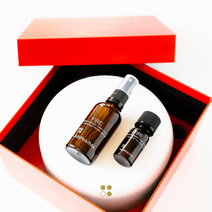 Een open rode doos bevat twee bruine flessen met zwarte etiketten; één is een Aroma Diffuser Geschenkbox - Fire van RainPharma, met een verstuiver.