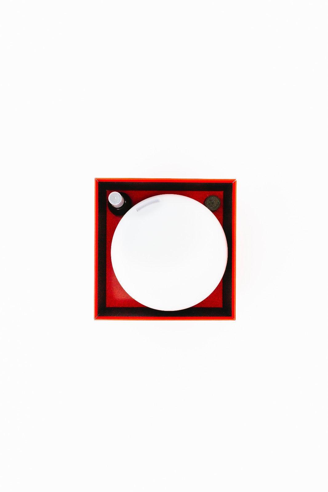 Een wit bord staat op een rood en zwart vierkant dienblad met daarnaast een klein donker schaaltje en een sausflesje. Dit doet denken aan de Aroma Diffuser Geschenkbox - Fire van RainPharma, van bovenaf bekeken.