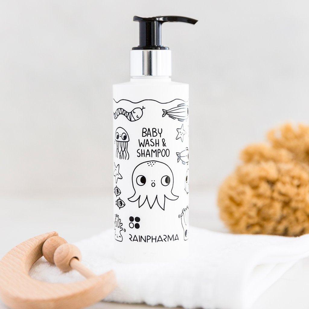 RainPharma Baby Wash & Shampoo 200 ml met illustraties van zwarte zeediertjes, afgebeeld op een witte handdoek naast een houten borstel en natuurlijke spons - perfect voor wie op zoek is naar hypoallergene babyproducten.