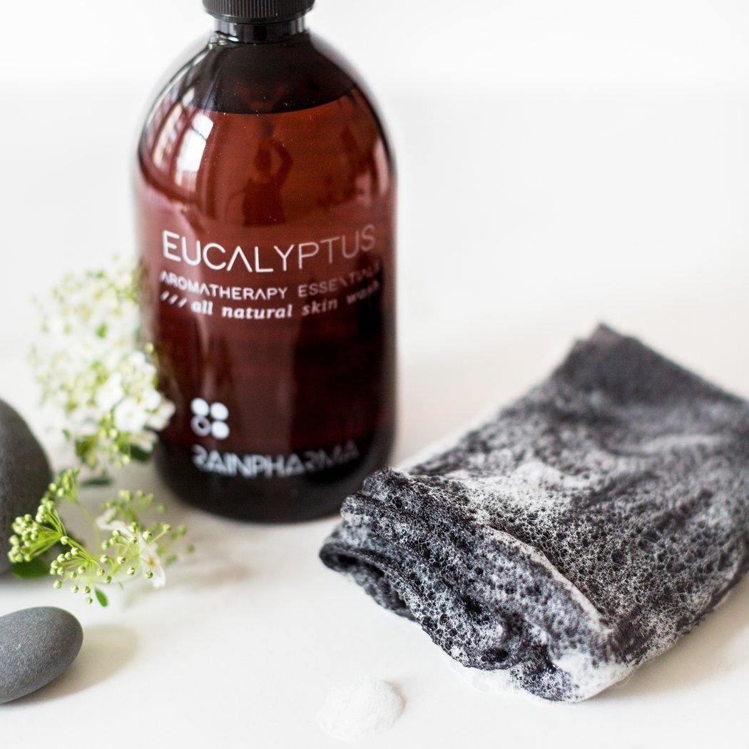 Een flesje etherische olie van eucalyptusaromatherapie staat naast delicate witte bloemen, gladde stenen en een RainPharma Body Wonder Towel voor een ongeëvenaarde ontspanningservaring.