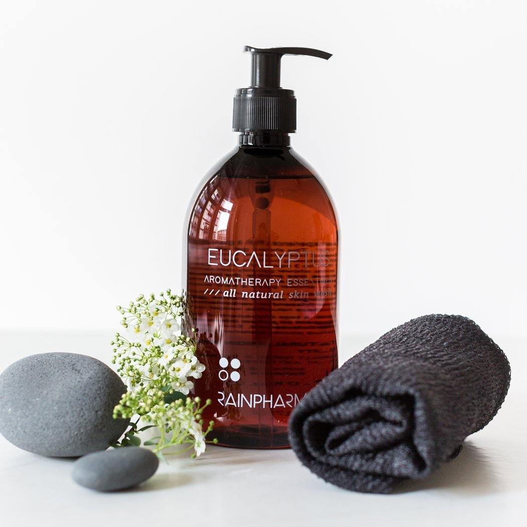 Een flesje etherische olie van eucalyptusaromatherapie ligt naast gladde stenen, een witte bloem en een zwarte handdoek op een wit oppervlak, aangevuld met de verjongende werking van de Body Wonder Towel van RainPharma.