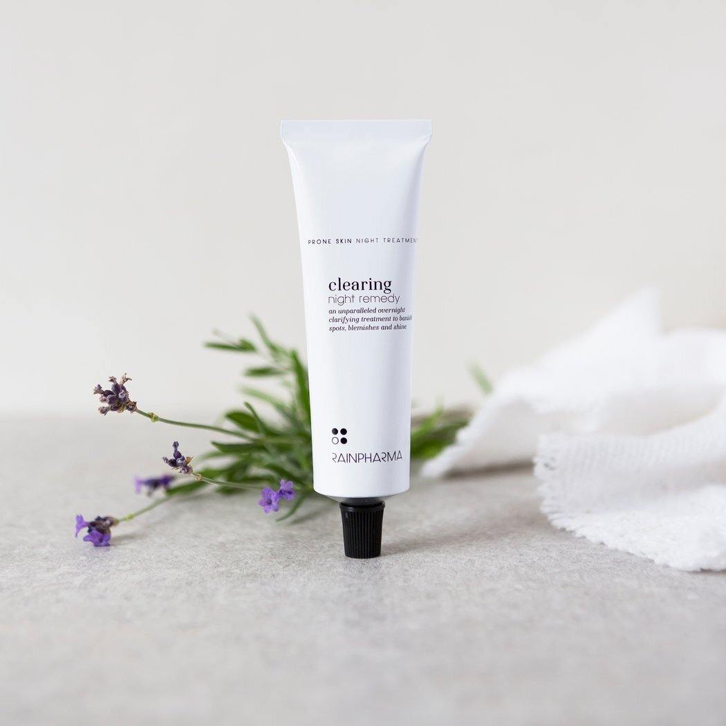 Een tube RainPharma Clearing Night Remedy - Dagcrème voor onzuivere of vette huid staat rechtop, omringd door lavendeltakjes en een witte doek, om de nachtverzorging met natuurlijke ingrediënten te benadrukken.