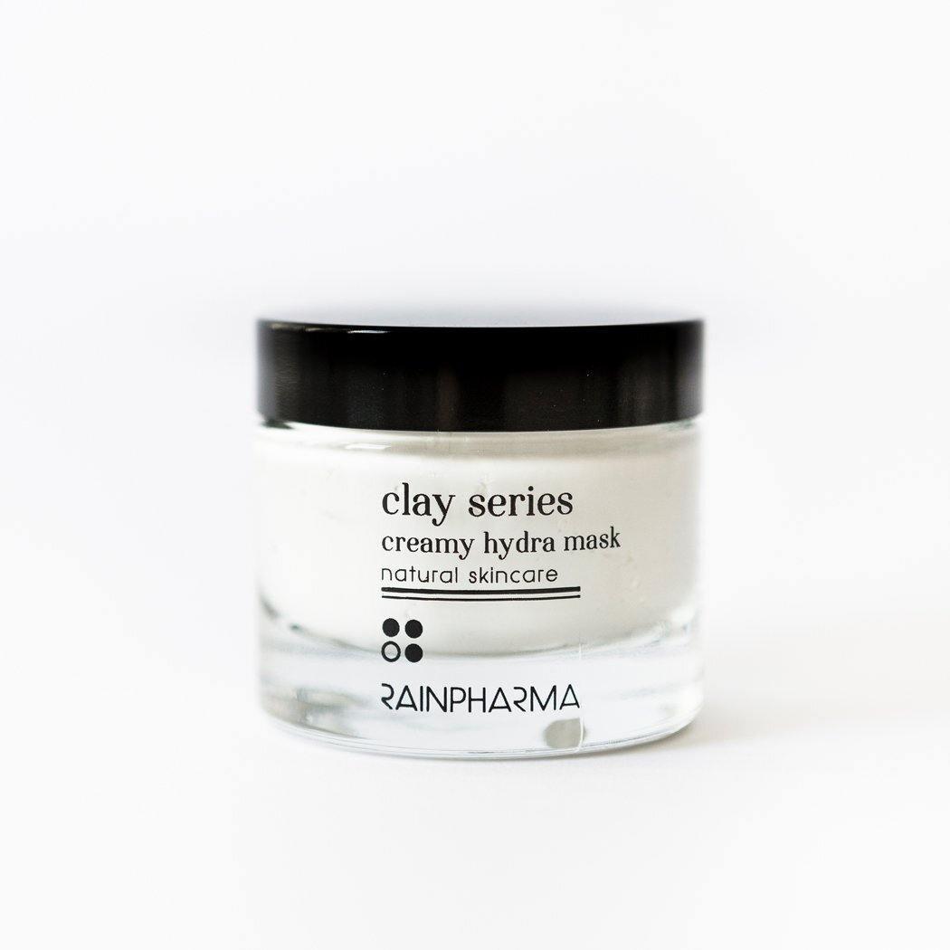 Een heldere glazen pot met een zwart deksel, met het opschrift "Creamy Hydra Mask - hydratatie masker" van RainPharma, wordt afgebeeld op een witte achtergrond.