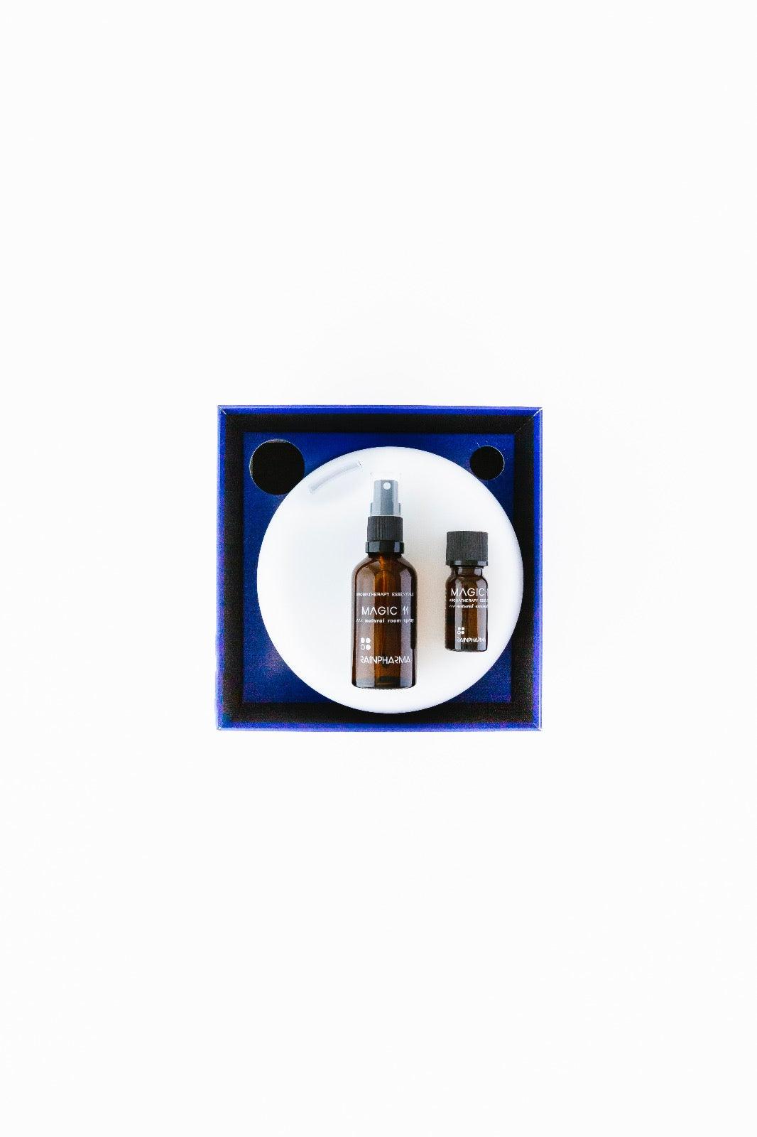 Twee bruine flessen met het opschrift "Magic" zitten in een blauwe rechthoekige doos met een witte ronde achtergrond, perfect ontworpen voor de Aroma Diffuser Geschenkbox - Magic 11 van RainPharma.