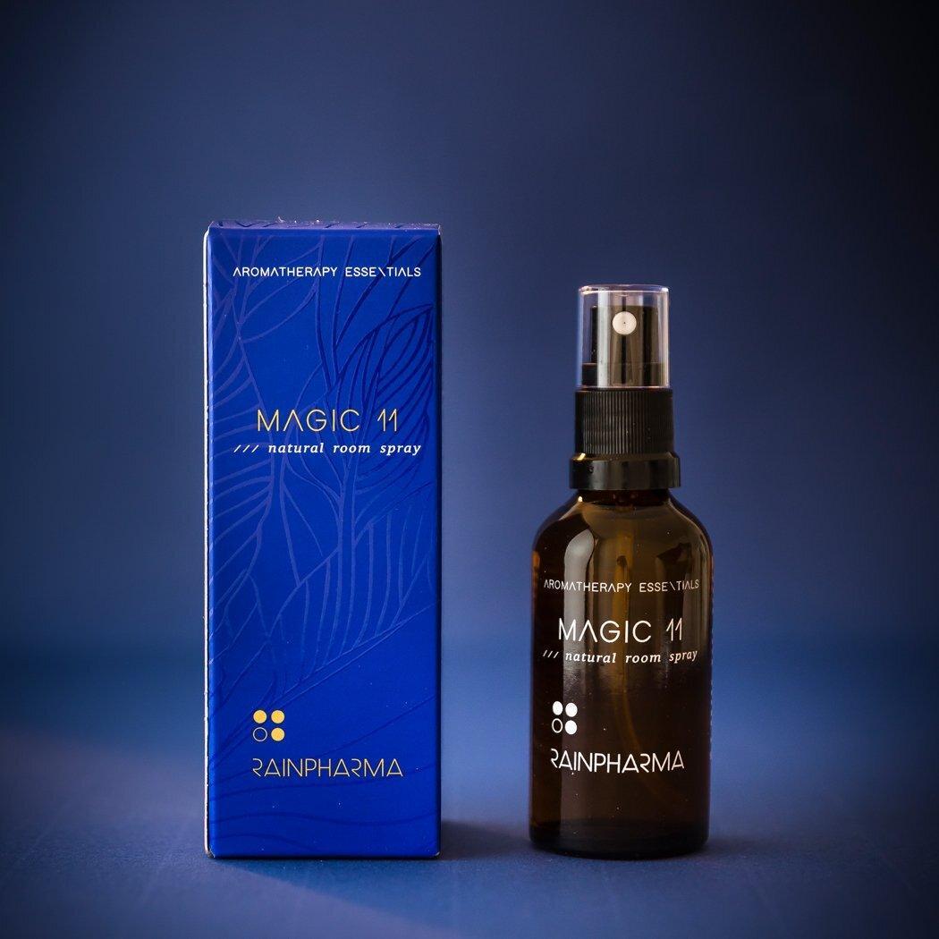 Een bruine sprayflacon met de tekst "Natural Room Spray - Magic 11" van RainPharma staat naast een bijpassende blauwe RainPharma doos, beide tegen een donkerblauwe achtergrond.