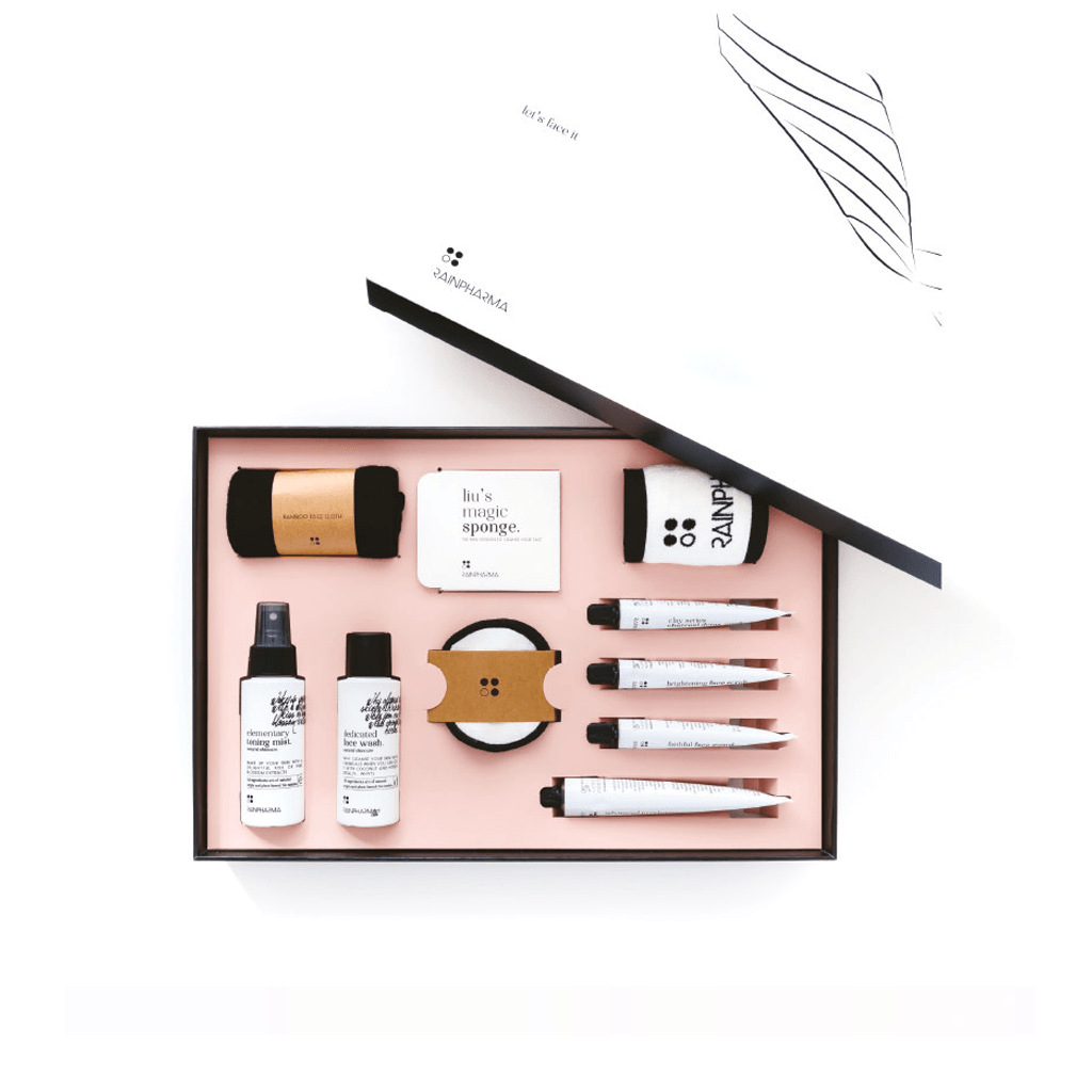 Een overzichtelijke skincare gift set in een open doos met flessen, tubes en accessoires op een roze dienblad. Ontdek de luxe Gelaatverzorging Set - Let&