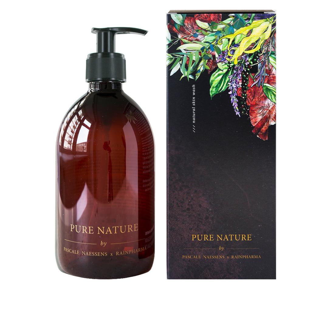 Een bruin pompflesje van Skin Wash Pure Nature van Pascale Naessens (RainPharma) staat naast een bloemig, bladerig doosje, ideaal om te combineren met een aromadiffuser of om te gebruiken als een heerlijke essentiële olie.