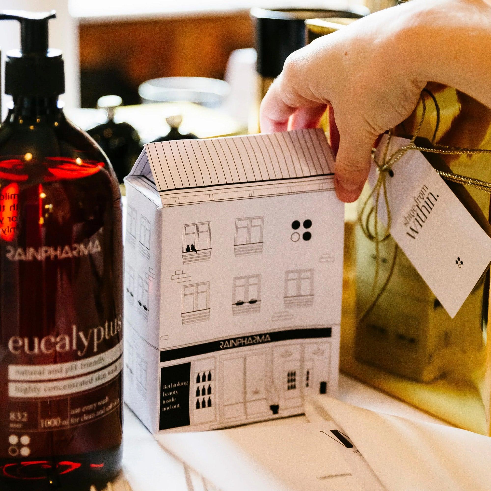 Een hand houdt een geschenkdoos vast in de vorm van een gebouw naast RainPharma&