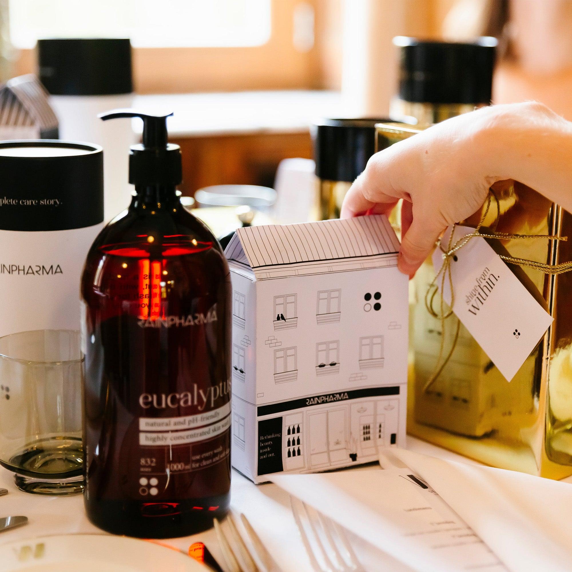 Een hand houdt een klein doosje vast in de vorm van een huis, naast een grote fles RainPharma&