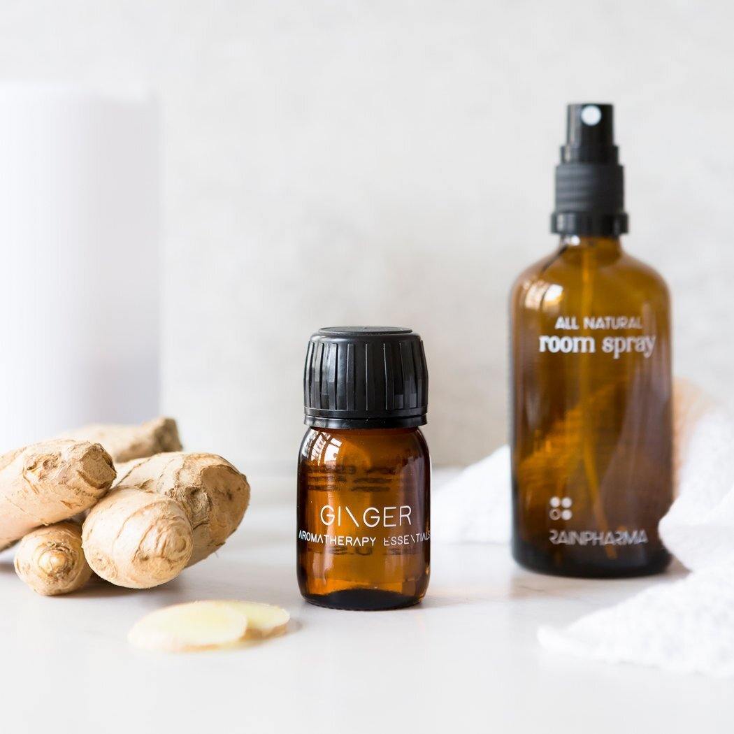 Amberkleurige flesjes met etherische olie van RainPharma - Gember, bekend om zijn therapeutische eigenschappen, en een volledig natuurlijke kamerverfrisser staan opgesteld met verse stukjes gember.