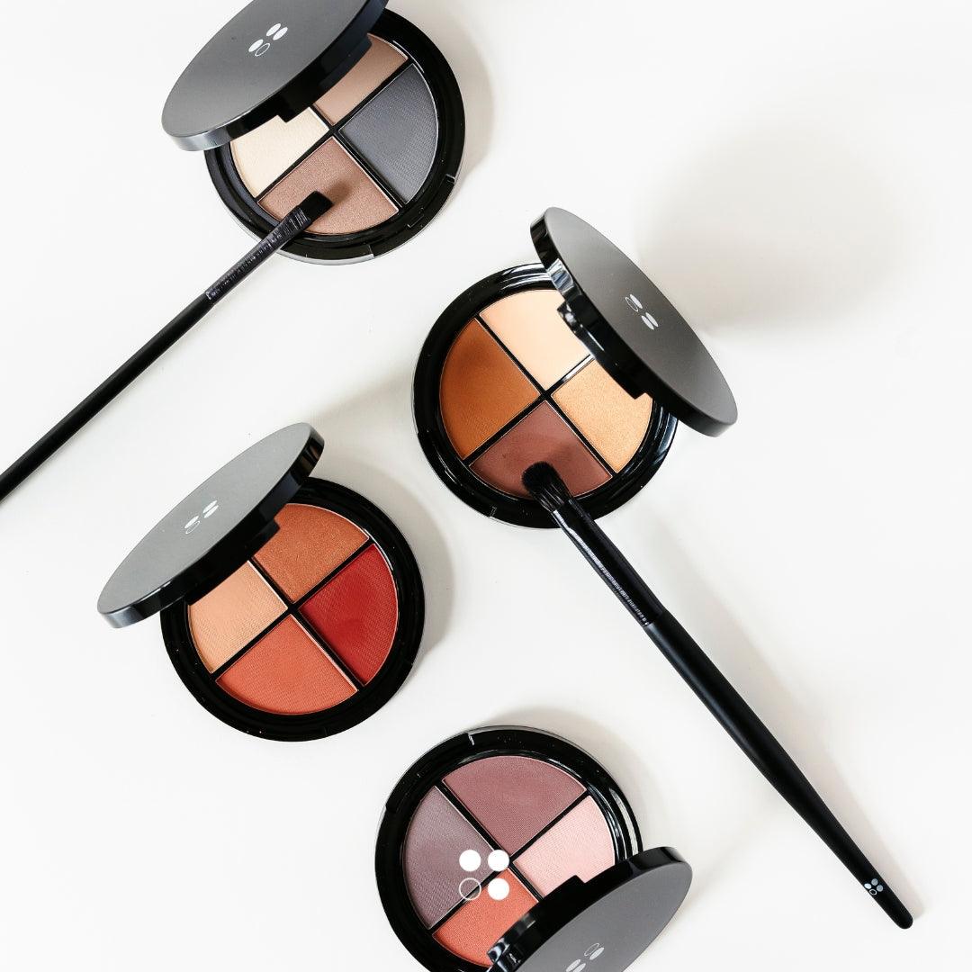 De Cadeaubon Make-up verwenmoment voor twee van Puur Living bevat drie zwarte oogschaduwpaletten met elk vier tinten (neutrale en warme tinten), afgebeeld op wit met twee kwasten, perfect voor liefhebbers van natuurlijke make-up.