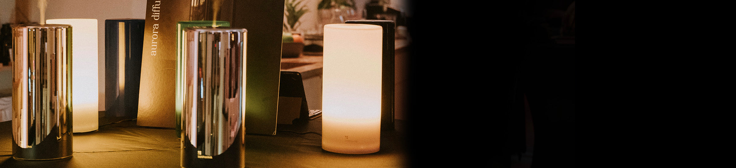 In een schemerige kamer staan op een tafel een aantal moderne metalen en cilindervormige lampen tentoongesteld.