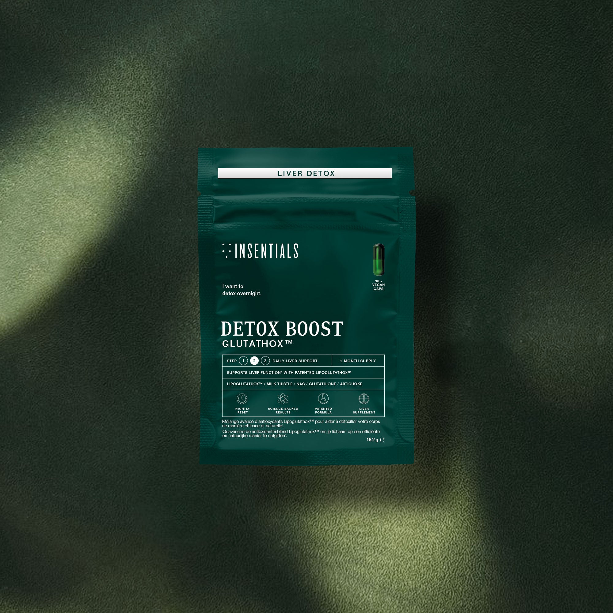 Een groen pakje met het opschrift „Insentials Detox Boost (leverontgifting en spijsvertering)” ligt op een donkergroen, gestructureerd oppervlak.
