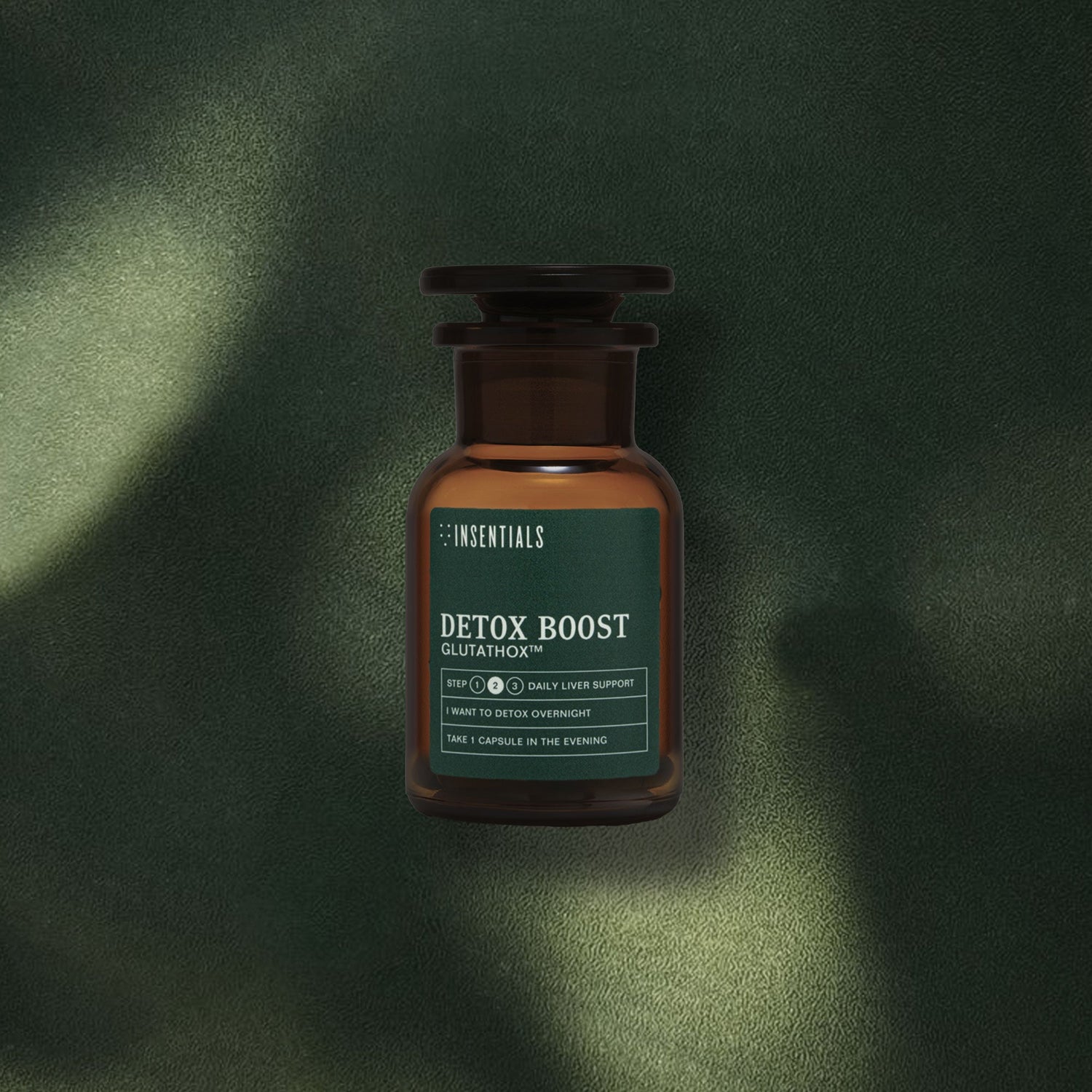 Een bruine glazen fles Detox Boost (leverontgifting en spijsvertering) van Insentials staat op een donkergroen, gestructureerd oppervlak, terwijl het licht de scène verlicht — ideaal voor wie zijn lever wil ontgiften en de spijsvertering wil ondersteunen.