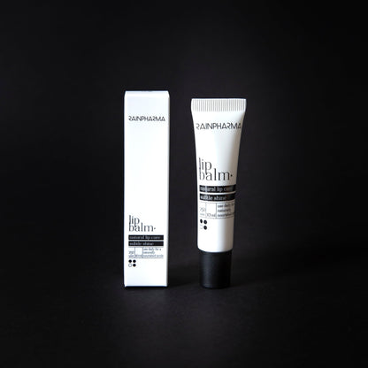 Een RainPharma lippenbalsem, verrijkt met plantaardige oliën, wordt naast de witte verpakking op een zwarte achtergrond getoond.