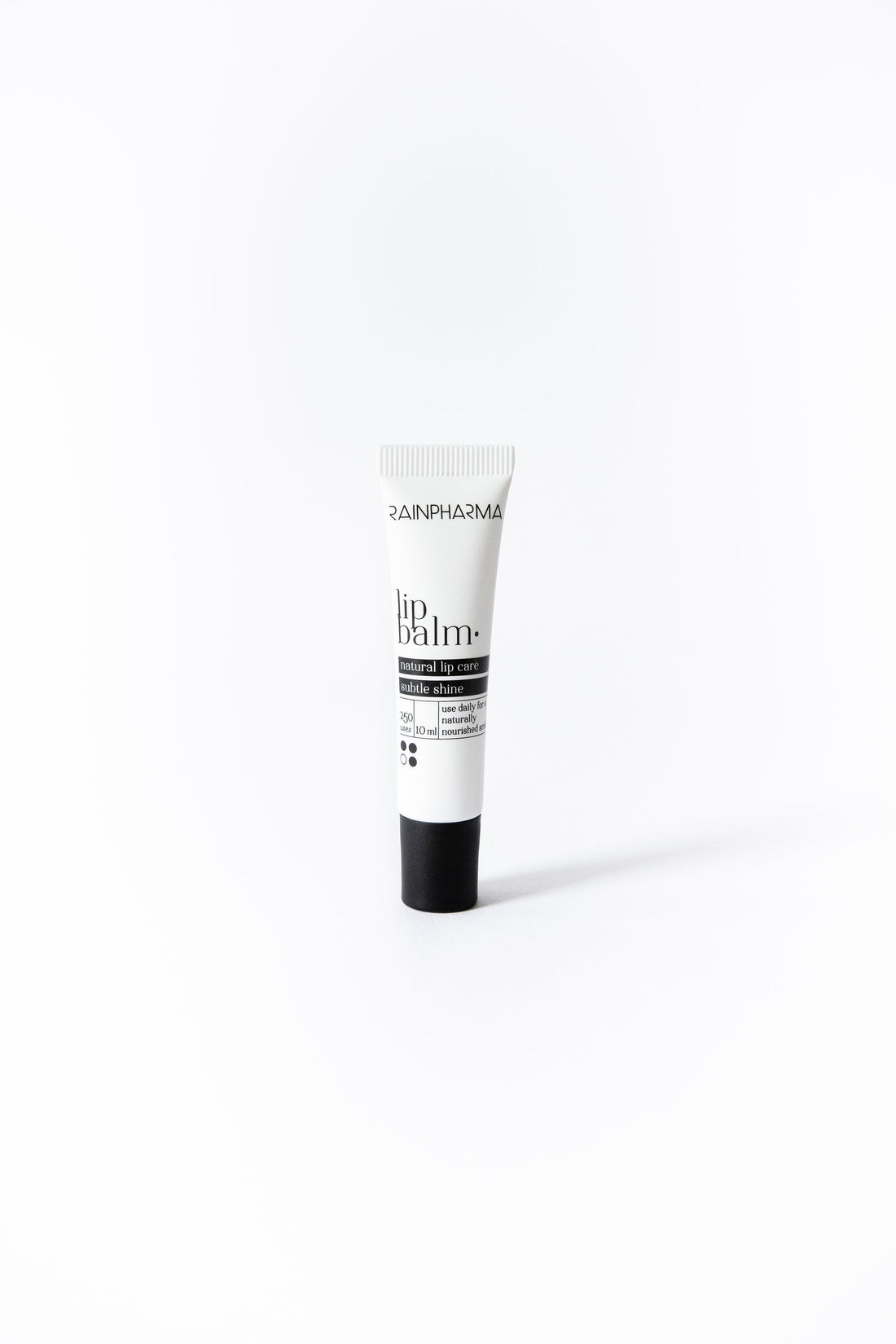 Een kleine tube RainPharma Lip Balm, met een witte body en zwarte dop, staat rechtop op een effen witte achtergrond. Geformuleerd met plantaardige oliën, hydrateert en verzacht het moeiteloos uw lippen.
