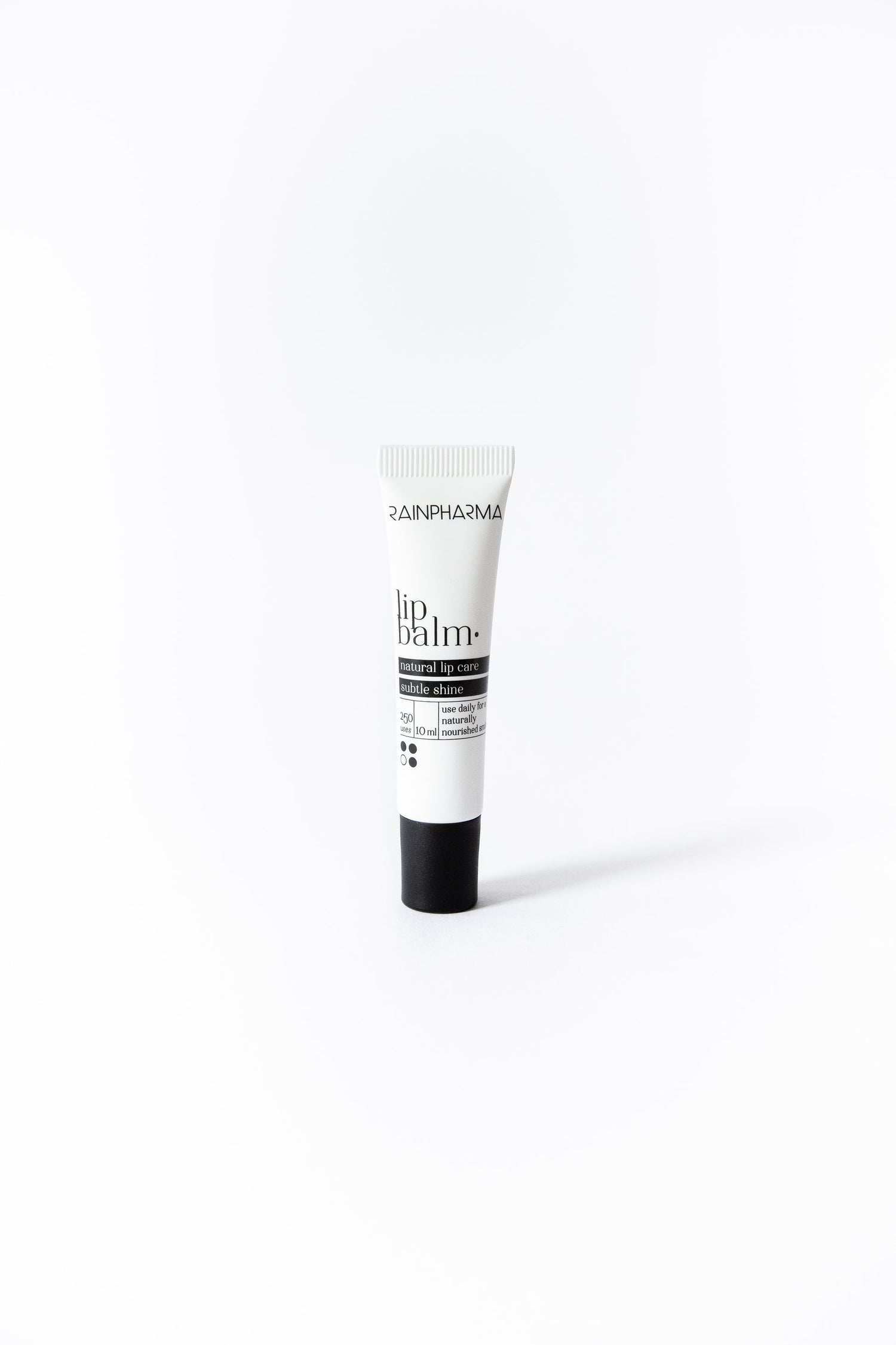 Een kleine tube RainPharma Lip Balm, met een witte body en zwarte dop, staat rechtop op een effen witte achtergrond. Geformuleerd met plantaardige oliën, hydrateert en verzacht het moeiteloos uw lippen.