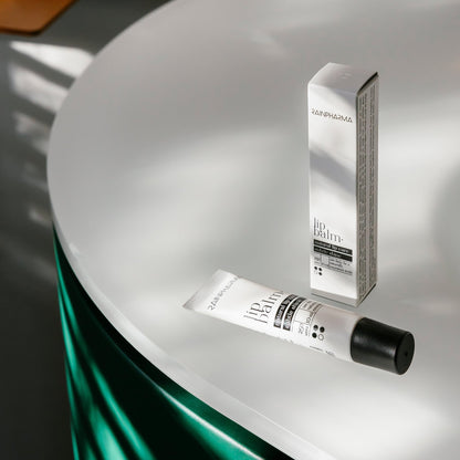 Een RainPharma lippenbalsem, verrijkt met hydraterende plantaardige oliën, is afgebeeld op een rond, wit oppervlak tegen een achtergrond van groene stof.