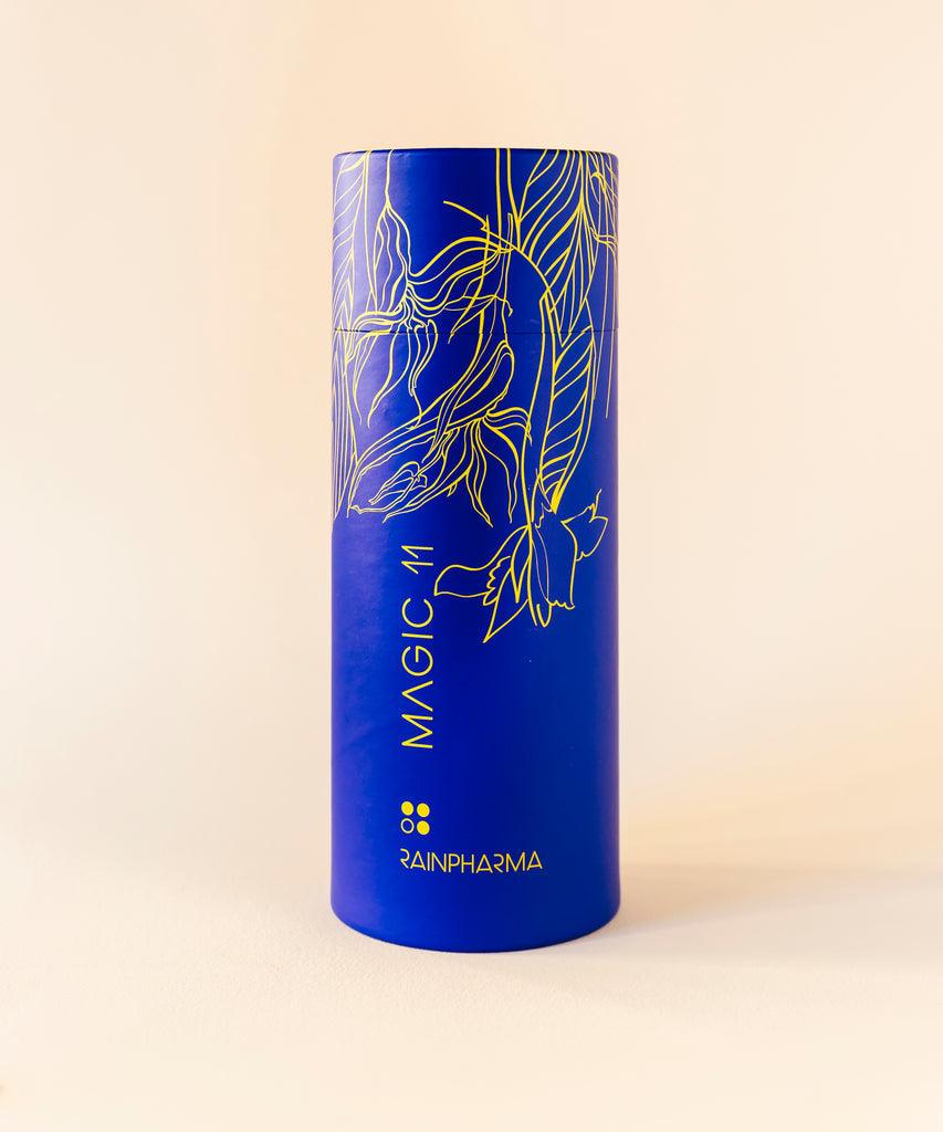 Een blauwe cilindrische container met het opschrift "Skin Wash Magic 11" van RainPharma, versierd met gouden bloemmotieven, bevat een plantaardige douchegel gemaakt van natuurlijke ingrediënten, geplaatst tegen een lichte achtergrond.