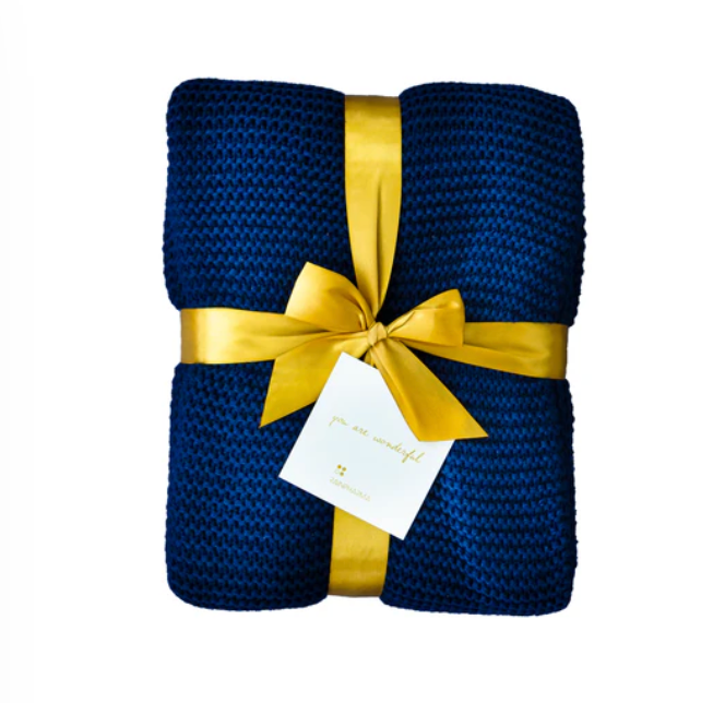 Een marineblauwe RainPharma luxe deken, zorgvuldig gebreid en elegant dichtgebonden met een gouden lint en strik, wordt geleverd met een maagdelijk wit kaartje.