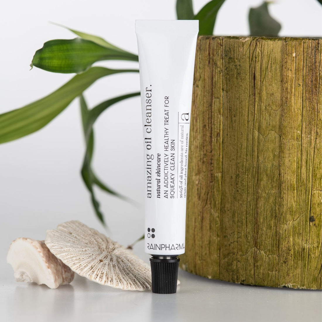 Een tube van 20 ml RainPharma Amazing Oil Cleanser, die zich richt op onzuiverheden voor een schone huid, wordt op een houten oppervlak gelegd met een plant en twee schelpen.