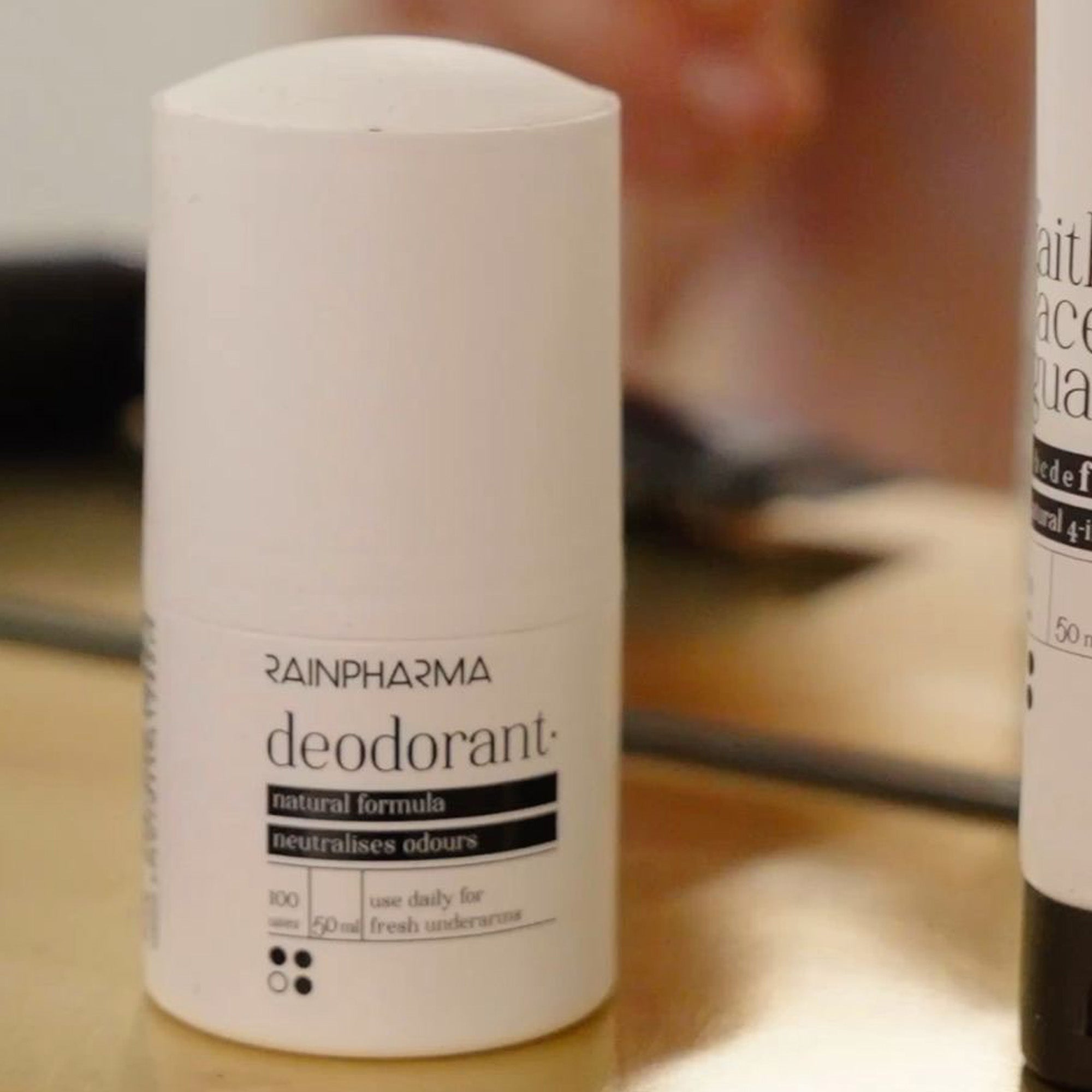 De NIEUWE! RainPharma - Deodorant, een witte stick met het label „natuurlijke formule”, staat op een reflecterend oppervlak naast een ander toiletartikel — zonder aluminiumzouten en microbioomvriendelijk voor milde, effectieve bescherming.