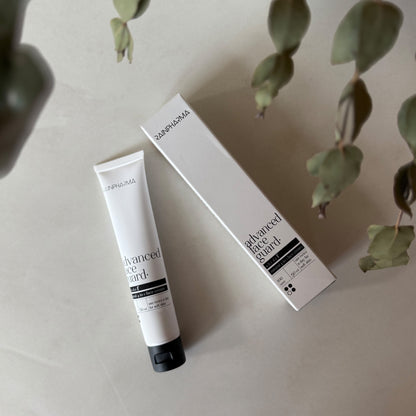 Een tube en het bijbehorende doosje met de tekst &quot;RainPharma Advanced Face Guard - NIEUW&quot; liggen op een licht oppervlak met groene bladeren in de buurt en laten de 4-in-1 gelaatscrème met rode algenextract voor geavanceerde huidverzorging zien.