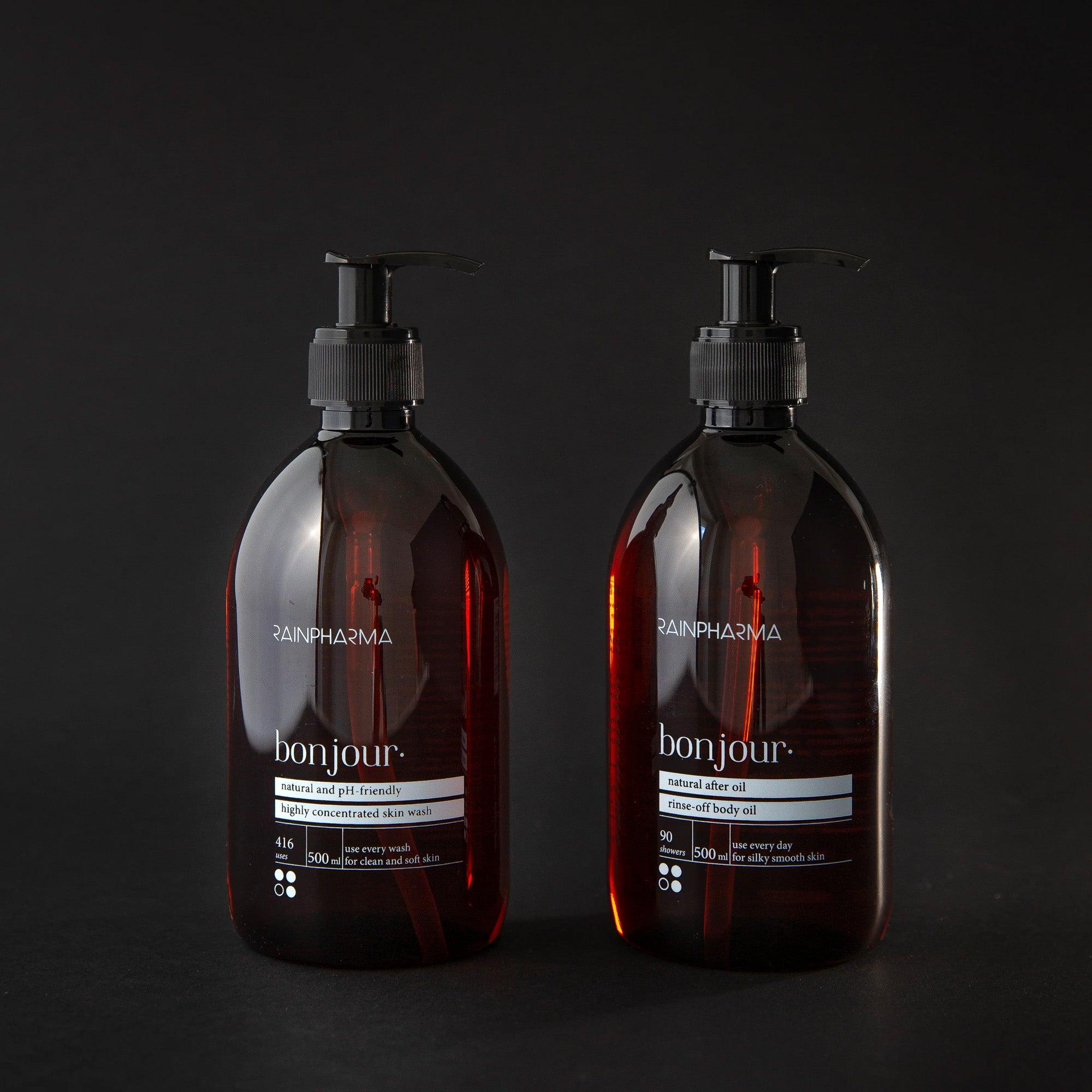 Twee flessen uit de RainPharma Doucheset - Bonjour Skin Wash + After Oil 500 ml, prachtig gepresenteerd tegen een donkere achtergrond. Ideaal als geschenkset voor een verkwikkende start van de dag.