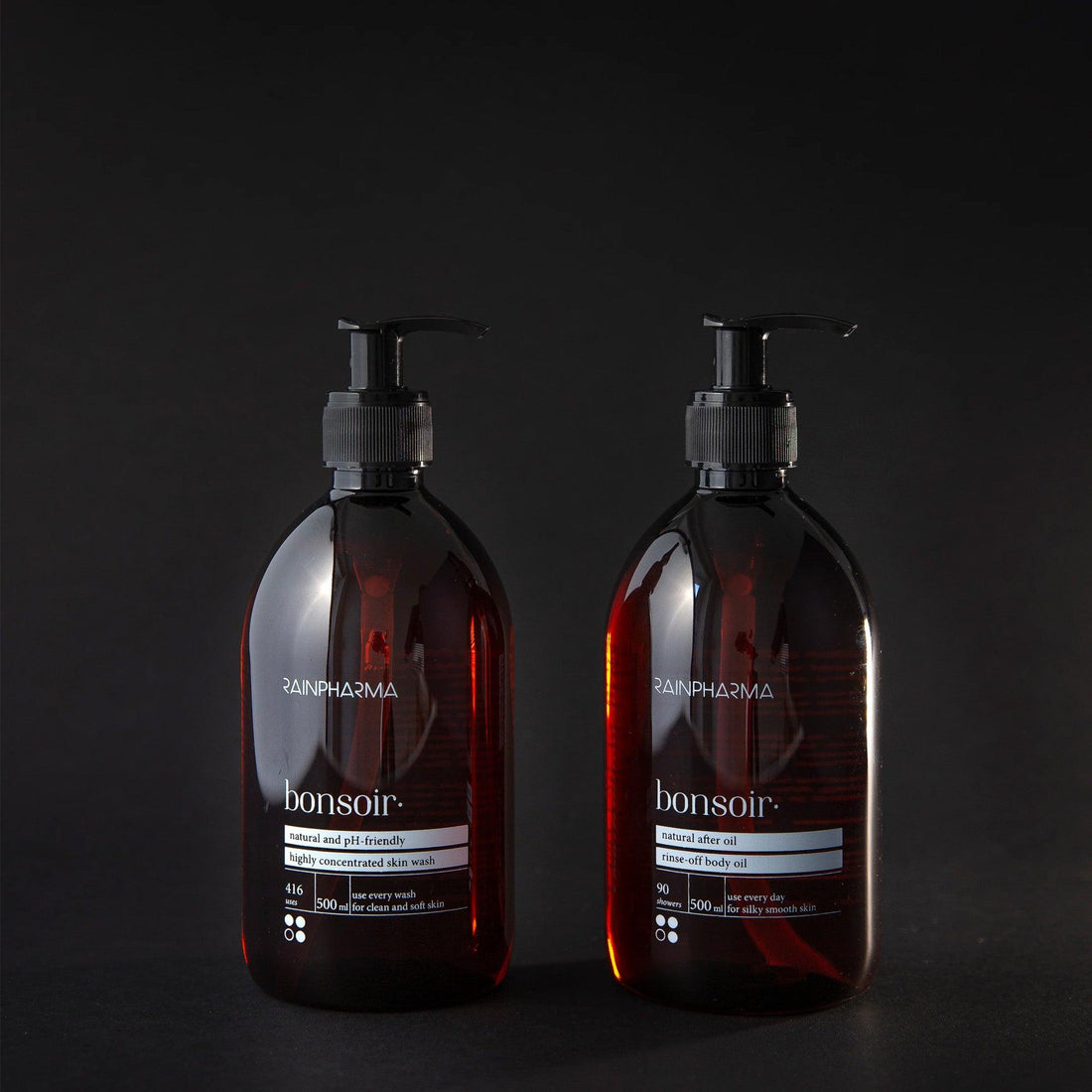 Twee pompflacons uit de RainPharma Doucheset, bestaande uit Bonsoir Skin Wash en After Oil (500 ml), staan elegant opgesteld tegen een donkere achtergrond en nodigen u uit om te genieten van de ontspannende geur.