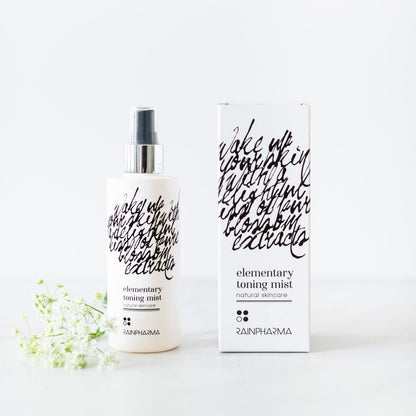 Een flesje en doosje RainPharma Toning Mist toner staan naast elkaar op een wit oppervlak, vergezeld van een klein takje witte bloemen.
