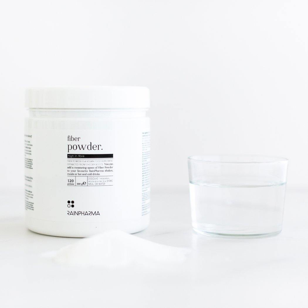 Een witte container met het opschrift &quot;Fiber Powder&quot; van Rainpharma naast een glas water op een schoon, wit oppervlak.