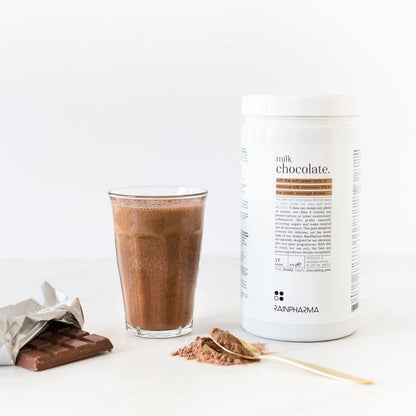 Een glas RainPharma Shake Melkchocolade, een reep chocolade en een bakje met het opschrift &quot;Rainpharma&quot; zijn kunstig gerangschikt op een wit oppervlak voor een eiwitrijk tussendoortje.