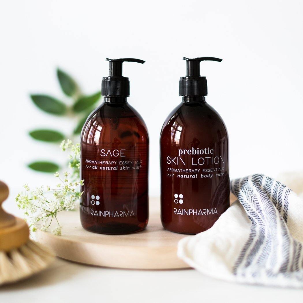 Een bruine pompflacon met het label "RainPharma Prebiotic Skin Lotion" staat op een houten dienblad met een handdoek, een borstel en groene bladeren - ideaal voor je prebiotische lotionroutine of plantaardige huidverzorging.