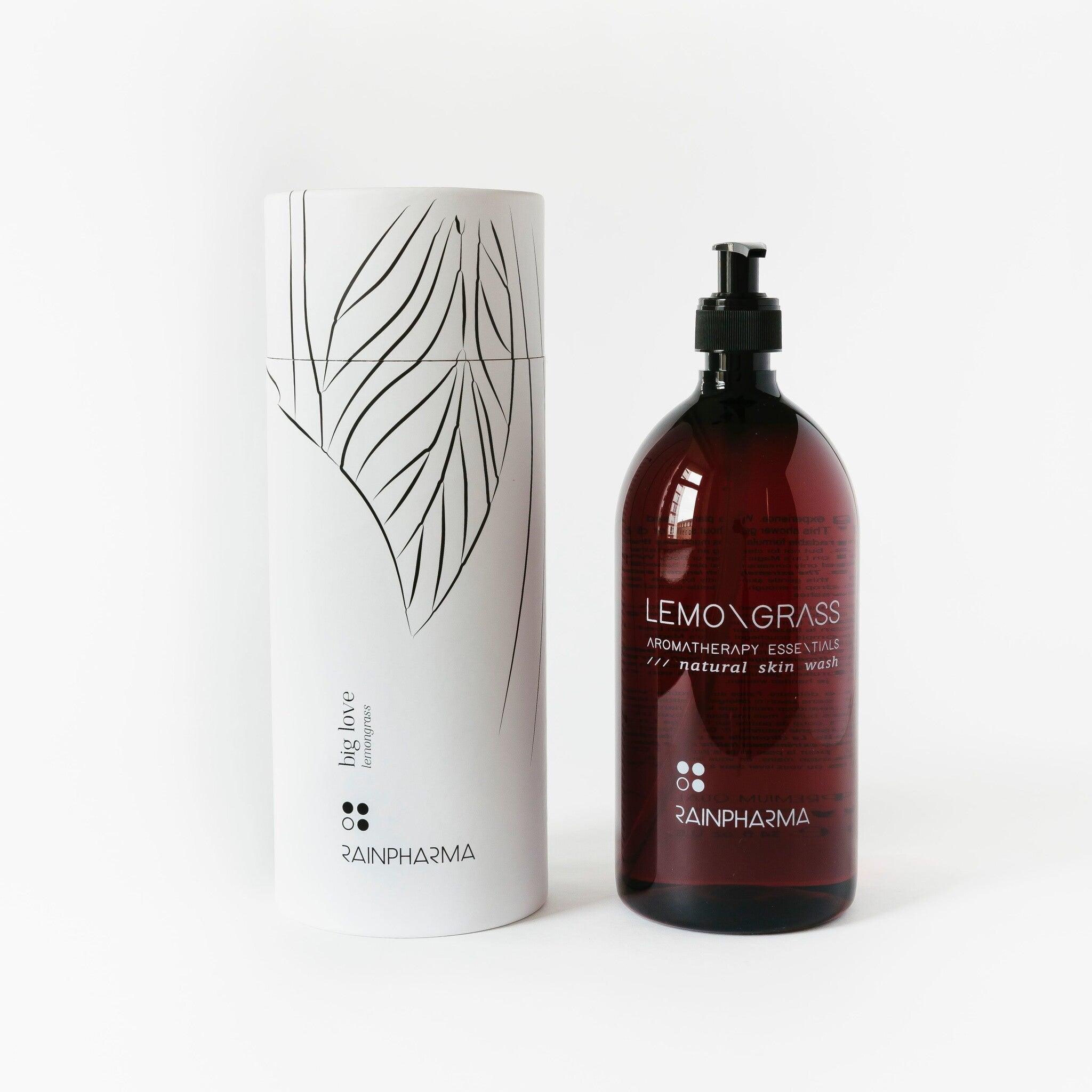 Een grote bruine fles met het label "Skin Wash Lemongrass" en een witte cilindervormige verpakking met een minimalistisch bladontwerp, beide van RainPharma, maken deel uit van de natuurlijke douchegel collectie van het merk.