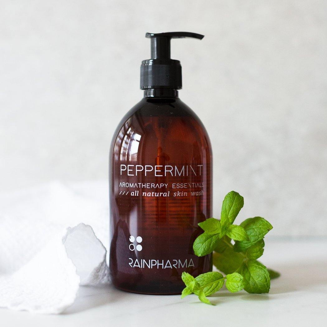 Een fles RainPharma Skin Wash Peppermint met pompje, naast verse munt en een witte handdoek; gemaakt van natuurlijke ingrediënten voor een milde reiniging.